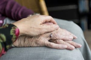 Angehörige hält die Hand einer pflegebedürftigen Seniorin