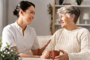 Nahaufnahme von Pflegekraft und Seniorin im persönlichen Gespräch mit Kaffee im Wohnzimmer